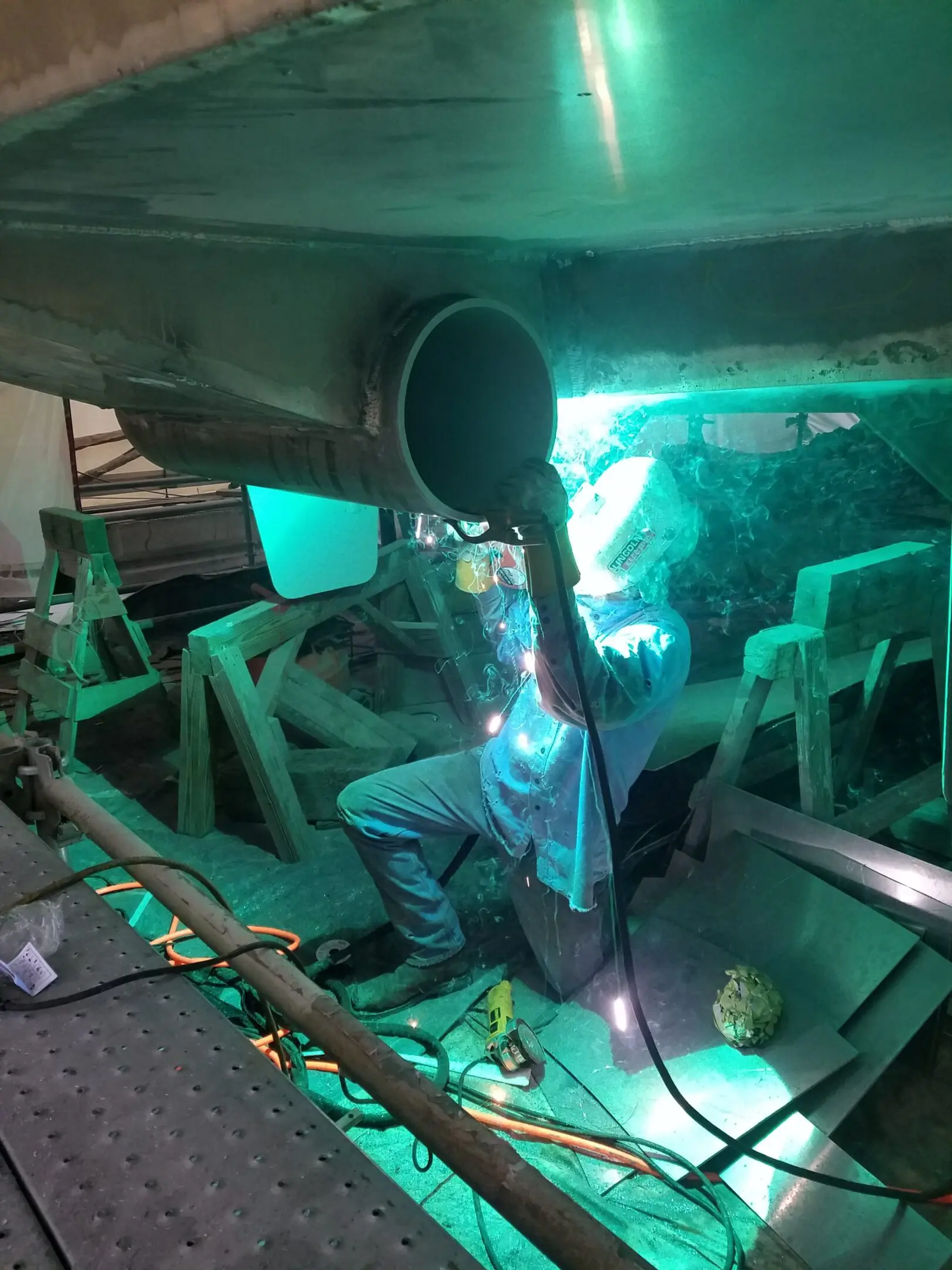 Person working under a car with green lighting and tools.