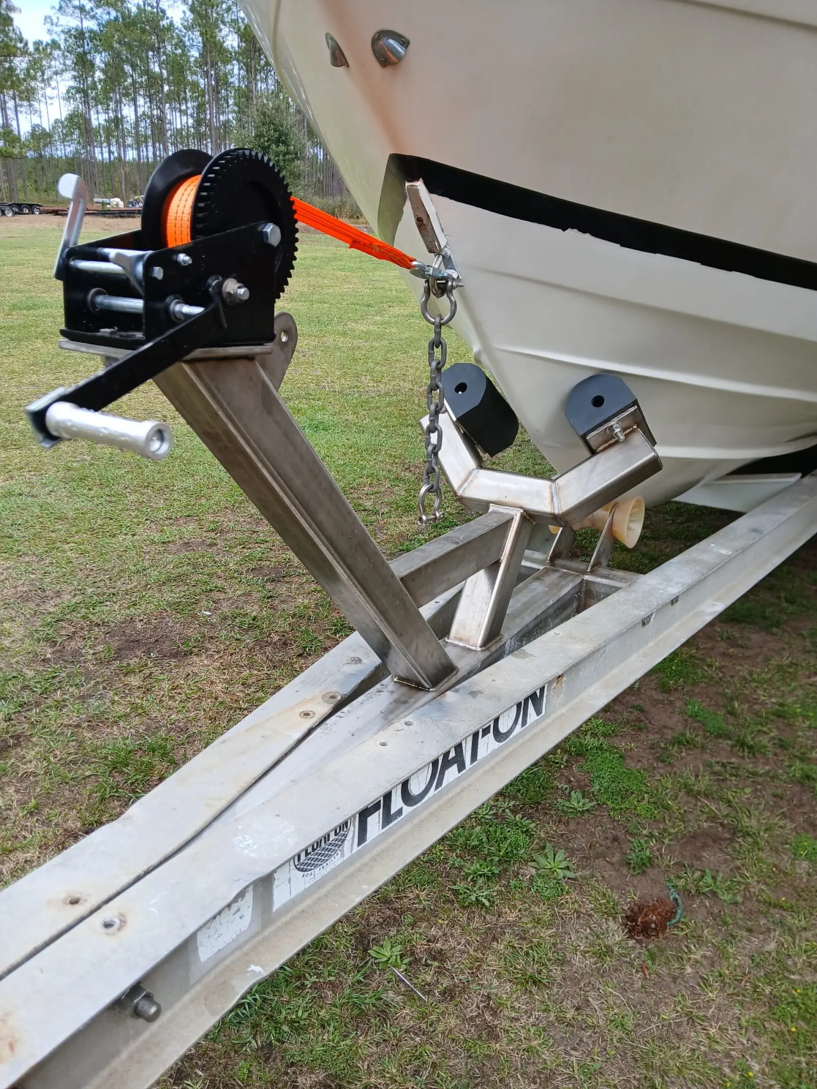 Boat trailer with winch and bow roller on grassy ground.