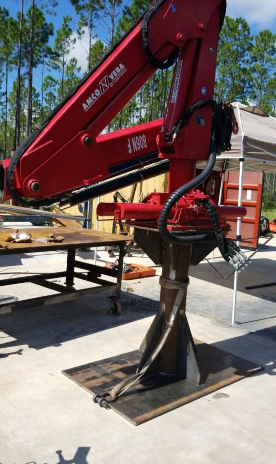 Red hydraulic crane arm lifting a heavy industrial auger attachment outdoors.